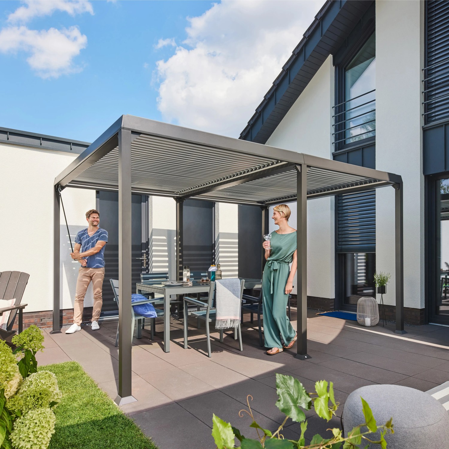 Home Deluxe Pavillon Cannes mit Lamellendach im Garten, mit Tisch und Stühlen.