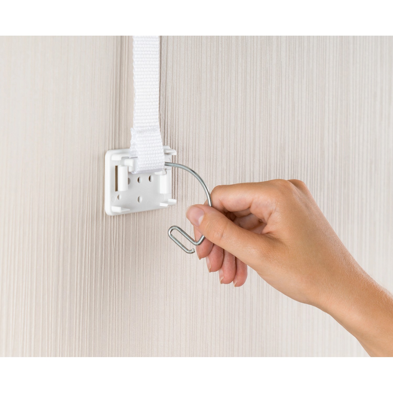 Reer Möbel-Kipp-Sicherung im Einsatz: Hand befestigt Haken am Gurtband. Kindersicherung für Möbel.