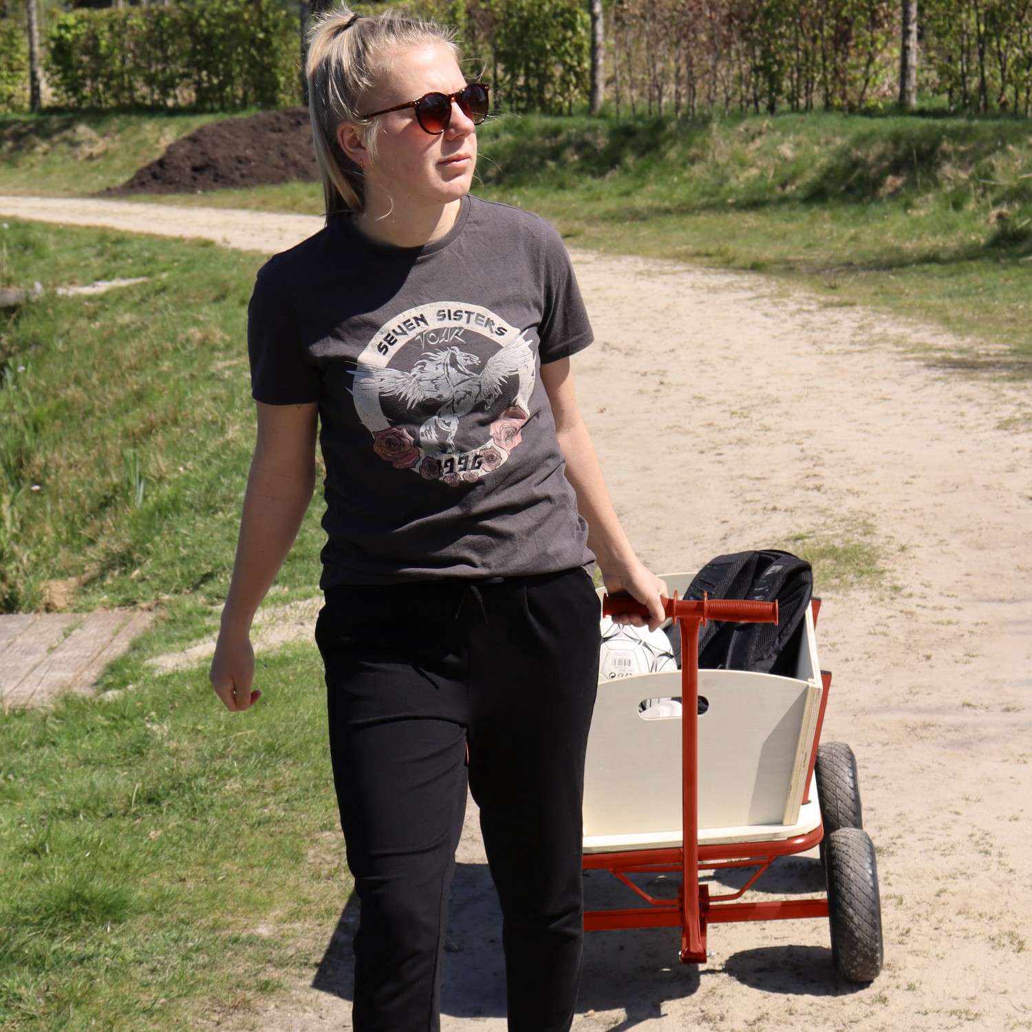 Frau zieht roten Sunny Bollerwagen Billy Beach Wagon mit Luftreifen auf einem Feldweg.