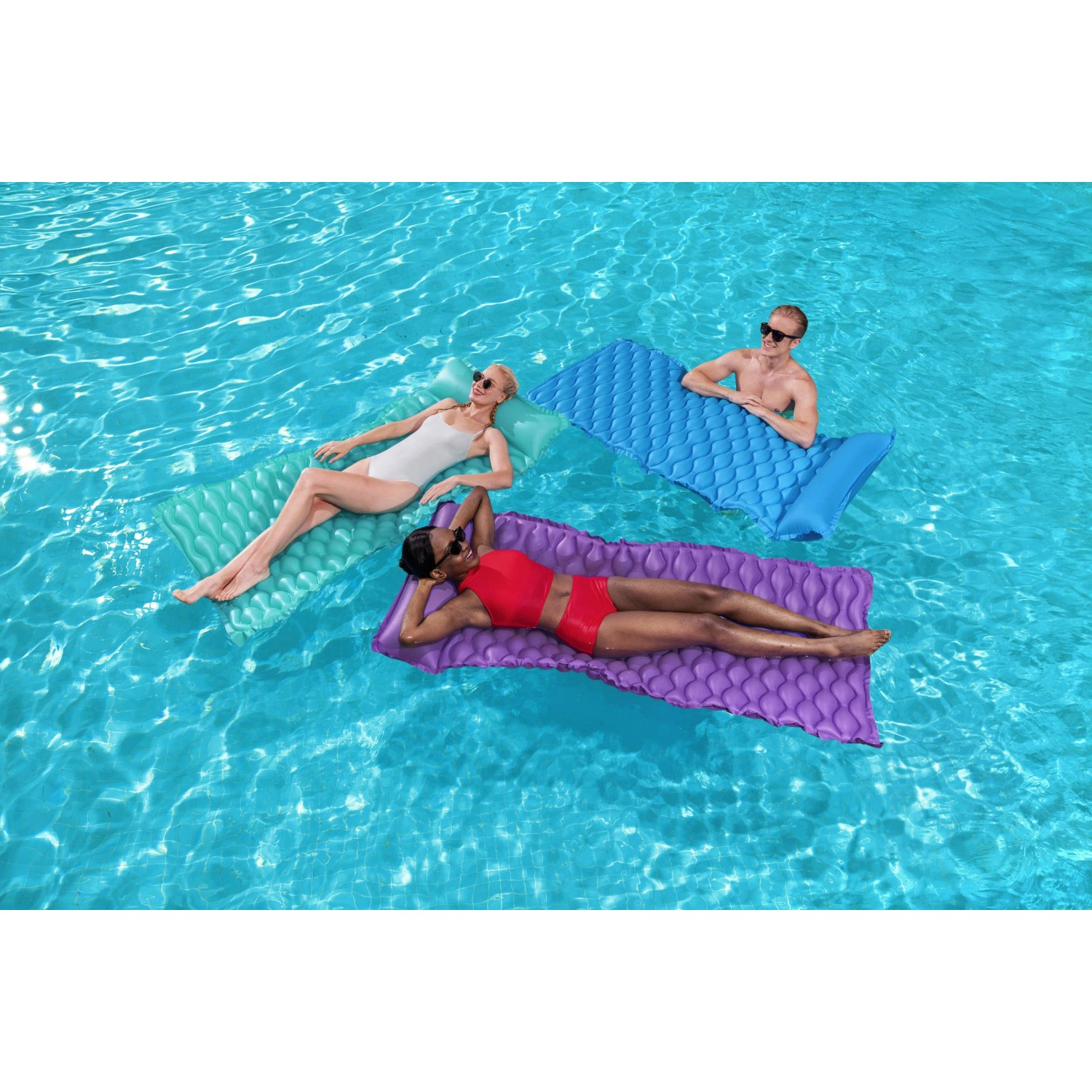 Drei Personen entspannen auf Bestway Luftmatratzen (blau, lila, grün) im Pool.