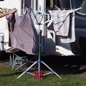 Mobile Alu-Wäschespinne mit blauen Gelenken. Person hängt Handtuch auf klappbaren Wäscheständer vor Wohnwagen.