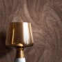 Strukturierte Vliestapete Savina mit bronzefarbenen Palmenblättern, Naturmotiv. Moderne Lampe im Vordergrund.