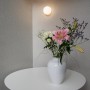 Marburg Vliestapete Uni Textiloptik grau-weiß an Wand mit Blumenarrangement.