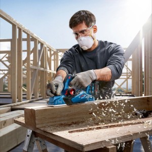 Mann hobelt Holz mit Bosch Akku-Hobel GHO 18V-26. Holzspäne fliegen. Präzises Hobeln von Holzbalken auf Baustelle.