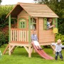 Axi Tom Spielhaus aus Holz mit roter Rutsche und spielenden Kindern im Garten.