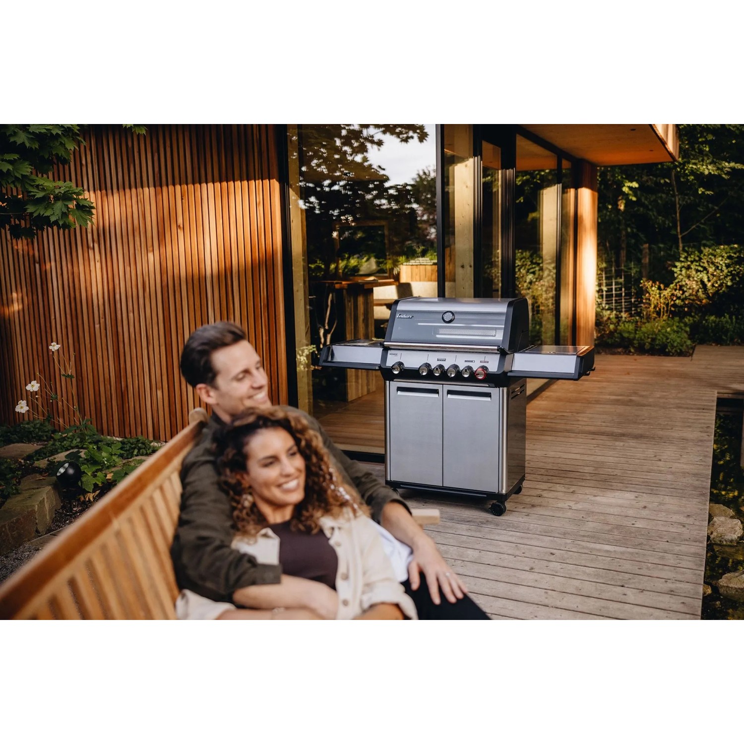 Enders Gasgrill Monroe Pro 4 SIKR Turbo mit Paar auf Holzterrasse. Edelstahl Gasgrill mit Seitenkocher.