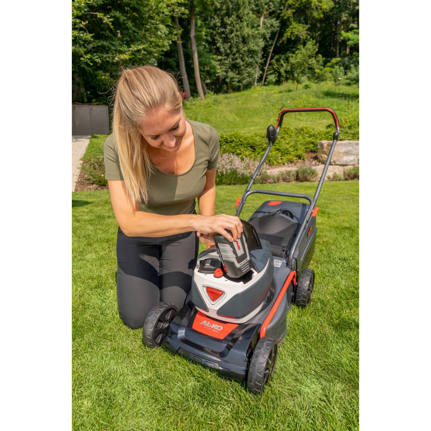 Frau setzt Akku in Al-Ko Akku-Rasenmäher 42.2 Li Comfort im Garten ein.