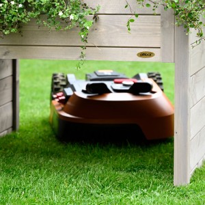 Graue Dobar Mährobotergarage mit Pflanzkasten und Mähroboter auf Rasen.