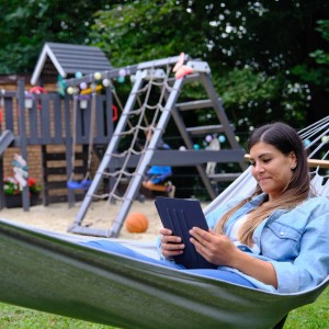 Frau entspannt in Hängematte vor Wickey Spielturm Smart Camp Klettergerüst im Garten.