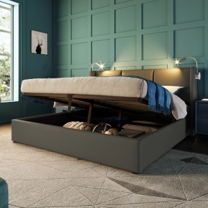 Graues Polsterbett 160x200cm mit hochgeklappter Matratze, die einen Bettkasten mit Stauraum zeigt. Kopfteil mit Leselampen und USB.