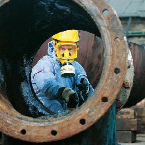 Gelbe Dräger X-plore 6570 Atemschutzvollmaske mit Filter an Arbeiter in Schutzanzug in rostiger Röhre.