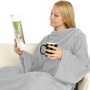 Frau mit grauer Bestlivings Kuscheldecke mit Ärmeln und Tasse auf dem Sofa.