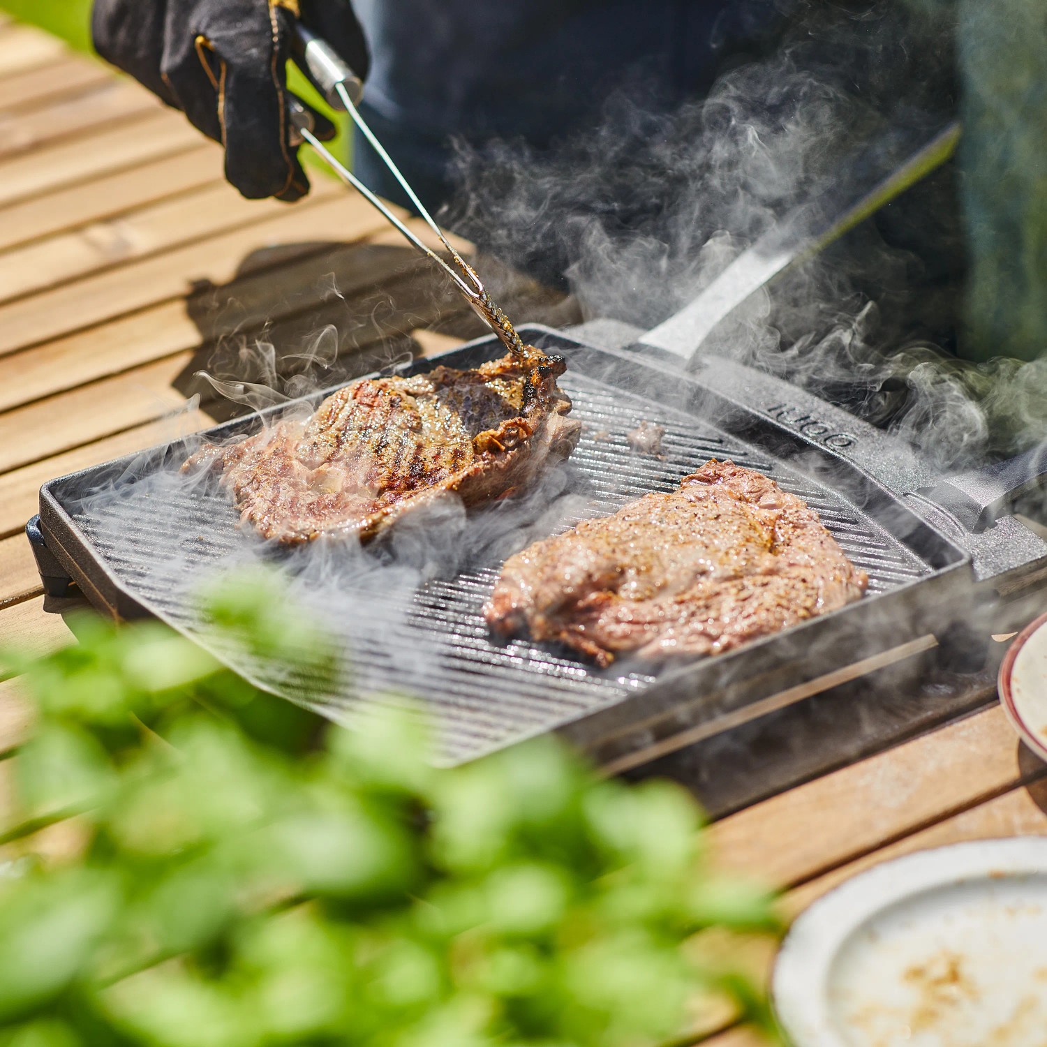 Ooni Grillpfanne Dual-Sided Grizzler mit Steaks auf Grillrippen. Gusseisen, doppelseitig, mit Dampf.