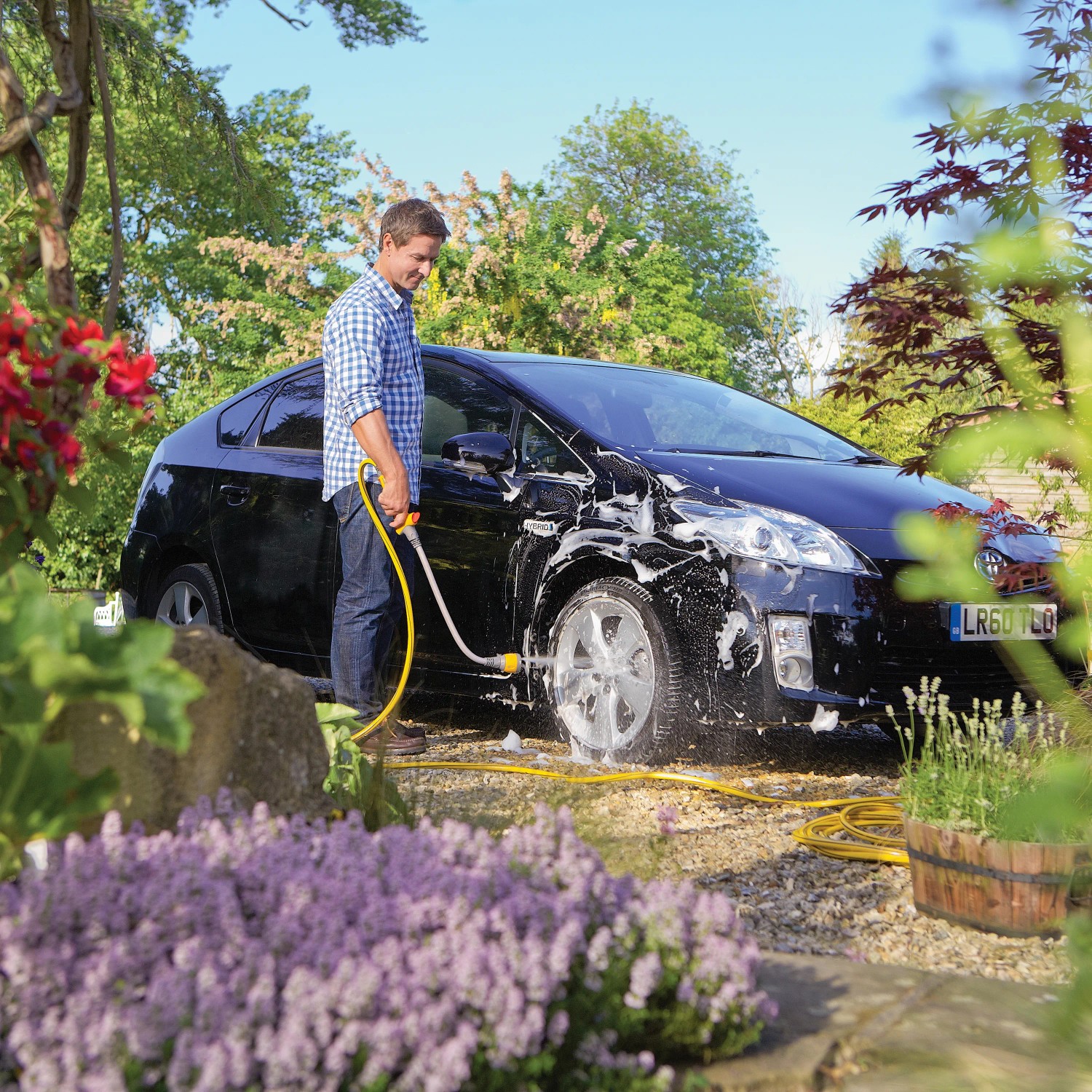 Mann wäscht Auto mit Hozelock Flexi Spray 4in1 Gartenbrause. Multifunktionale Wasserbrause mit flexiblem Korpus.