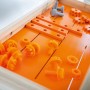 Zubehör für OBI Kinderwerkbank: orangefarbene und graue Spielzeugschrauben, Zahnräder, Holzleisten.