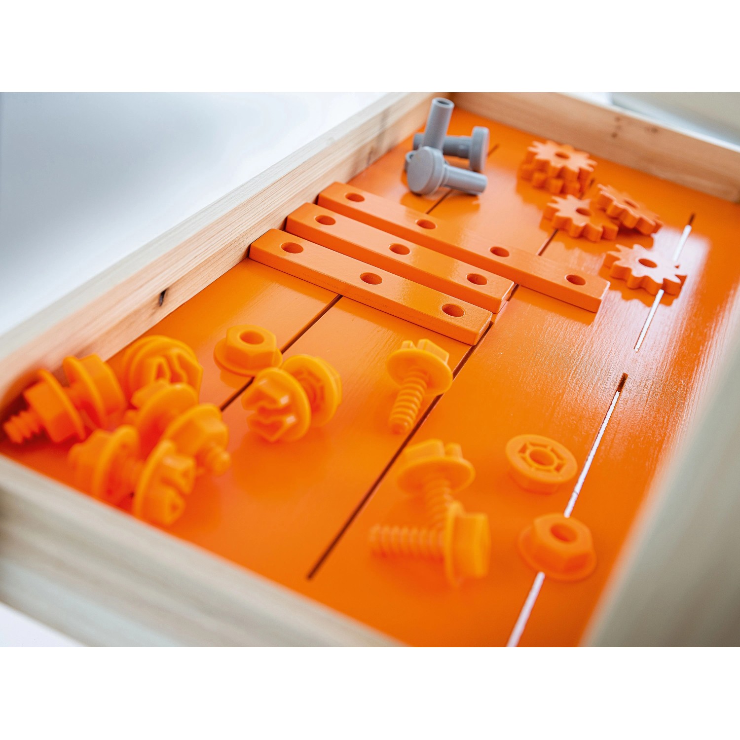 Zubehör für OBI Kinderwerkbank: orangefarbene und graue Spielzeugschrauben, Zahnräder, Holzleisten.