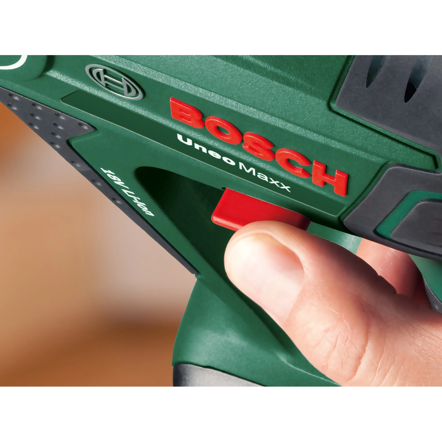 Detailaufnahme: Hand betätigt roten Schalter am grünen Bosch 18V Akku-Bohrhammer Uneo Maxx.