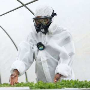 Dräger Pac 6000 Sauerstoff-Messgerät am Schutzanzug einer Person mit Atemschutzmaske in Arbeitsumgebung.
