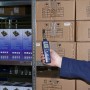 PCE Instruments Hygrometer 555 in Hand vor Lagerregal mit Kartons. Messwerkzeug zur Feuchtigkeitsmessung.