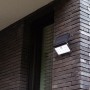 Schwarze LED Solar-Wandleuchte Tuda von Lutec mit Bewegungsmelder an einer Backsteinwand.