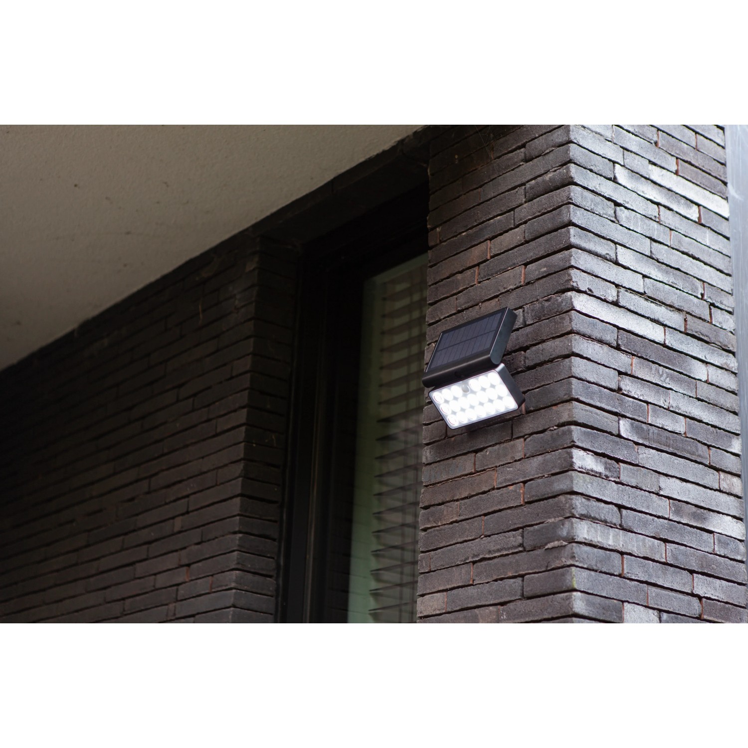 Schwarze LED Solar-Wandleuchte Tuda von Lutec mit Bewegungsmelder an einer Backsteinwand.