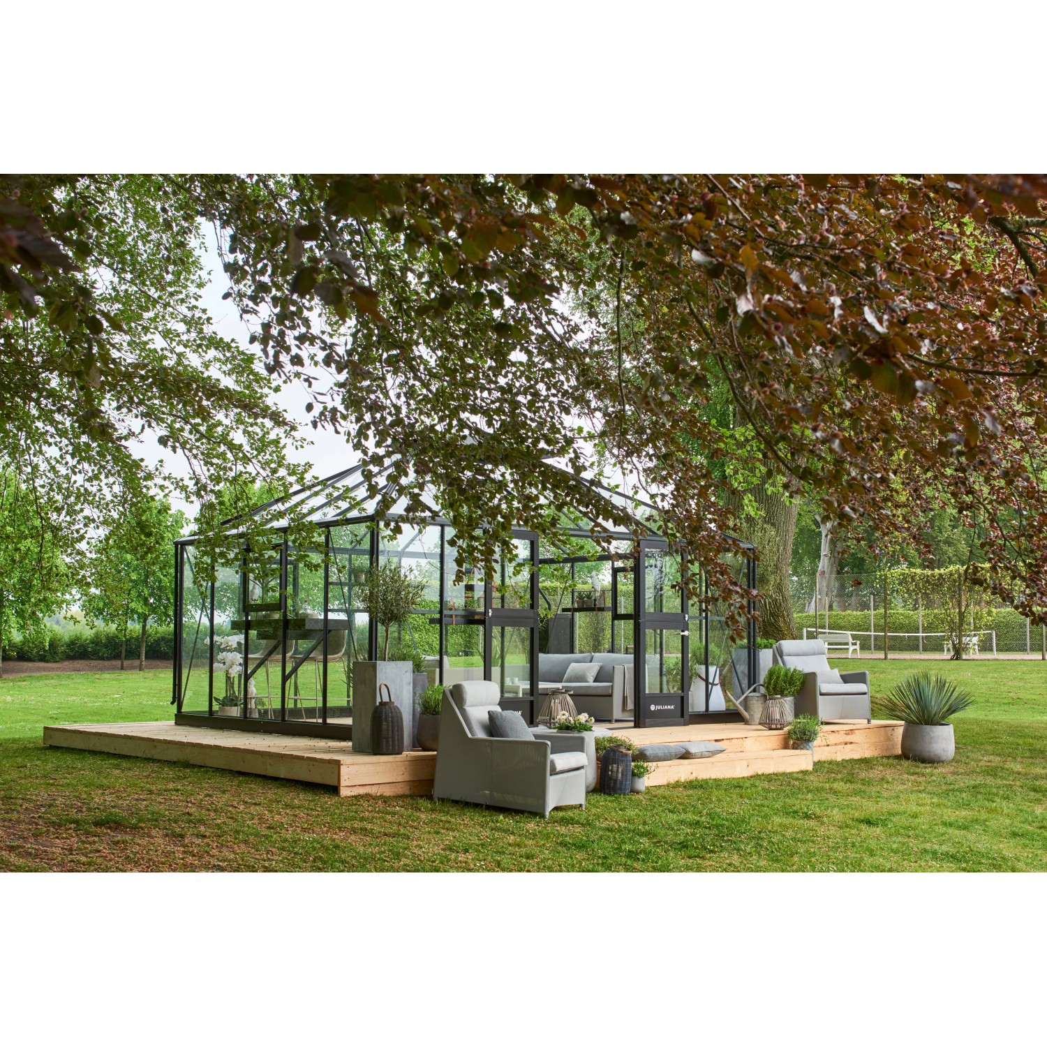 Juliana Gewächshaus Grand Oase 18 Anthrazit mit Sitzgruppe auf Holzterrasse im Garten.