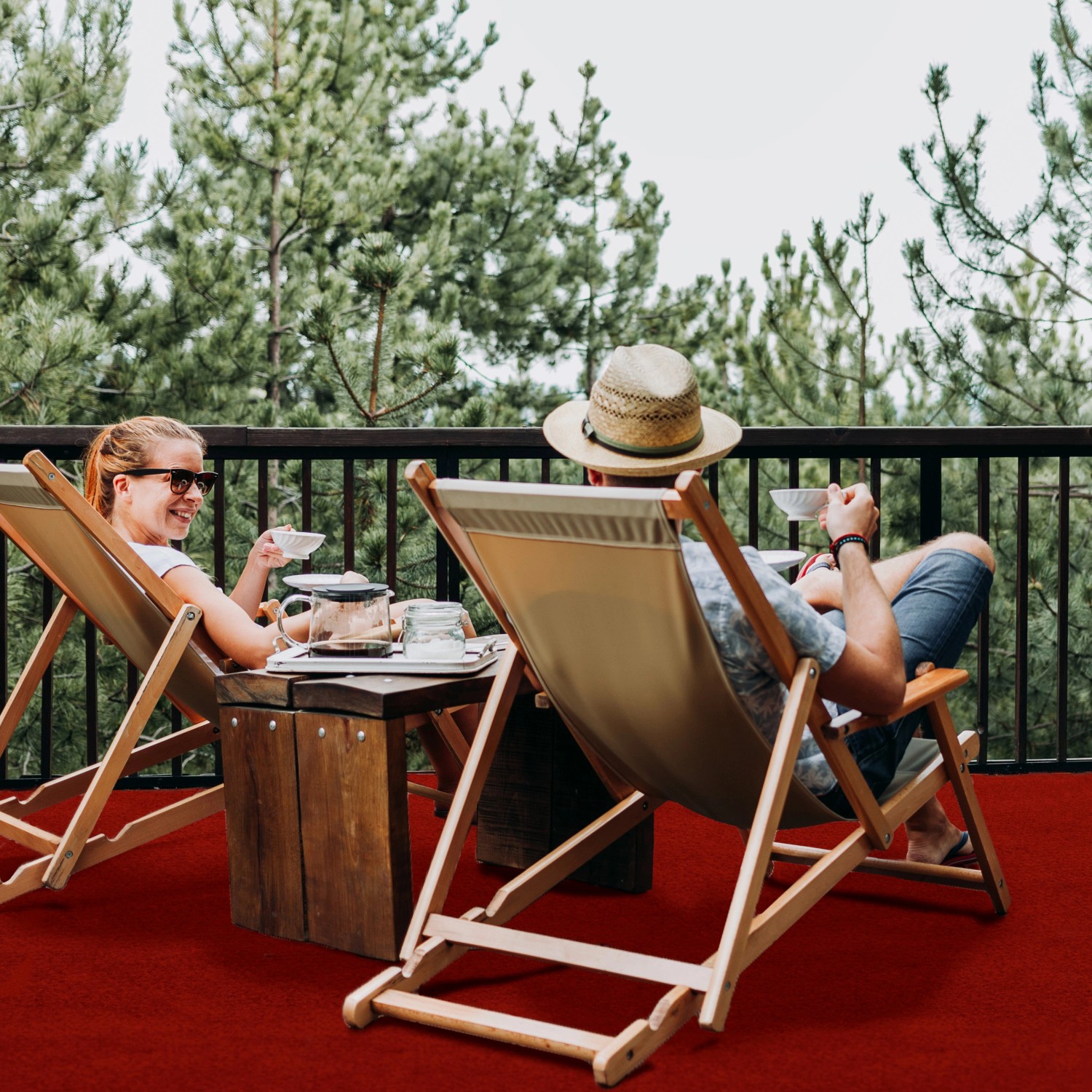 Roter Primaflor Rasenteppich auf Terrasse mit entspannten Personen in Liegestühlen.
