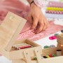 Offenes, ausklappbares Nähkästchen aus hellem Holz mit bunten Garnrollen. Eine Person näht im Hintergrund. Ideal zur Nähzeug Aufbewahrung.