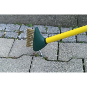 Florasun Unkrautfugenbürste mit gelbem Stiel und grüner Bürste im Einsatz auf Pflastersteinen.