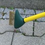 Florasun Unkrautfugenbürste mit gelbem Stiel und grüner Bürste im Einsatz auf Pflastersteinen.