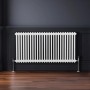 Weißer Monstershop 2-Säulen Heizkörper (600x1192mm) vor dunkler Wand auf Holzboden.