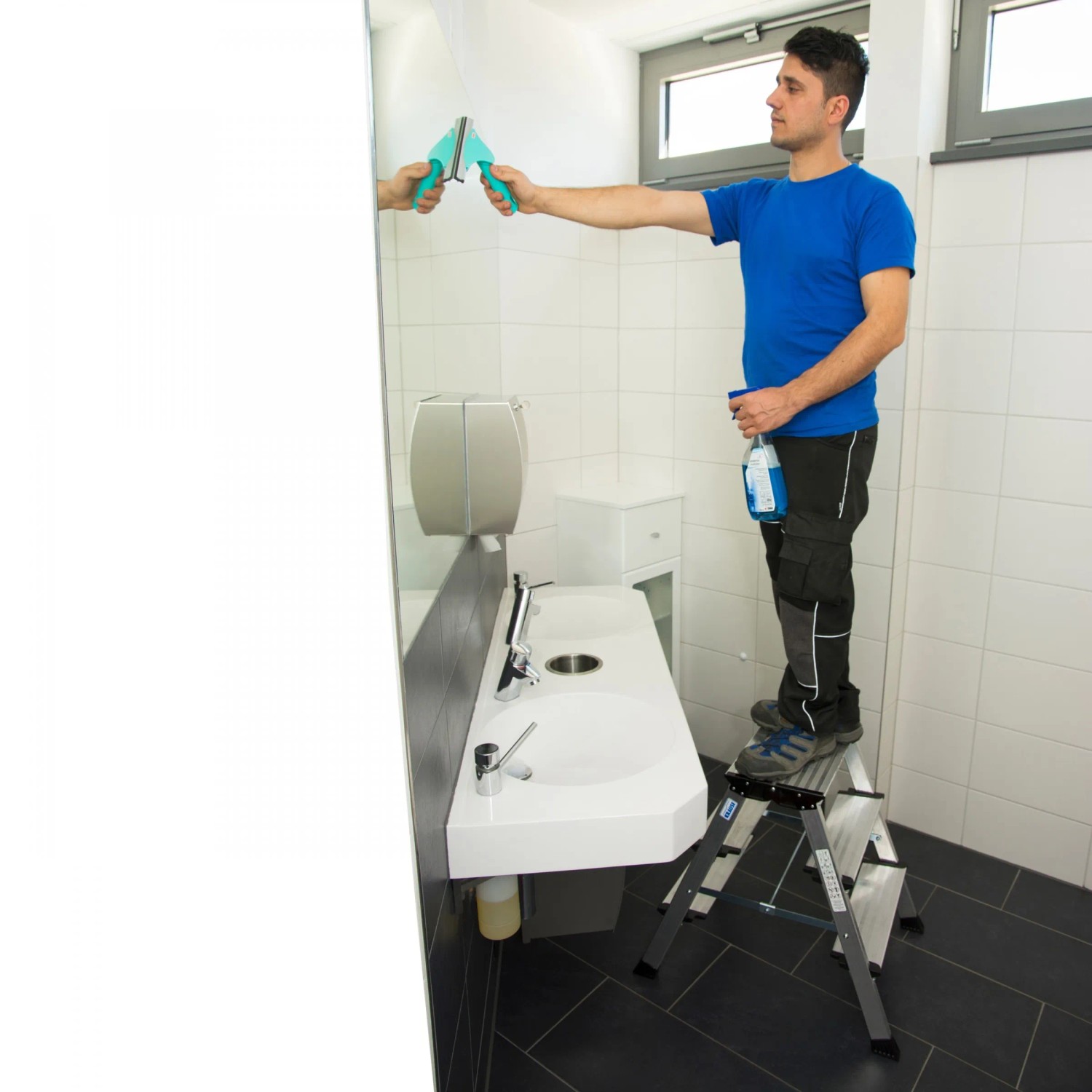 Mann reinigt Spiegel stehend auf Krause Treppo Klapptritt 2x3 Stufen Leiter.