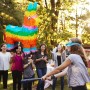 Bunte Lama Pinata aus Papier hängt im Garten. Eine Person schlägt blind mit Schläger, Kinder schauen zu. Perfekt für Geburtstagsparty & Partyspiel.