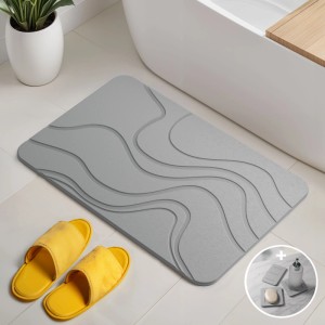 Graue Björn&Schiller Kieselgur Badematte 60x39 cm mit Wellenmuster vor Badewanne. Set mit Seifenschale & Untersetzern.