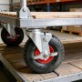 Schwarze luftbereifte Schwerlast-Lenkrolle aus Gummi/Stahl mit roter Nabe und Bremse, auf Transportwagen.