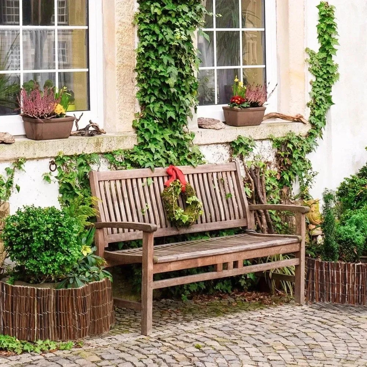 Flexible Weide Beeteinfassung als niedriger, geflochtener Zaun um Pflanzen, neben einer Holzbank im Garten.
