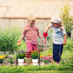 Kinder gießen Blumen mit einer Relaxdays Blumenbank im Garten. Zubehör für Pflanztöpfe.