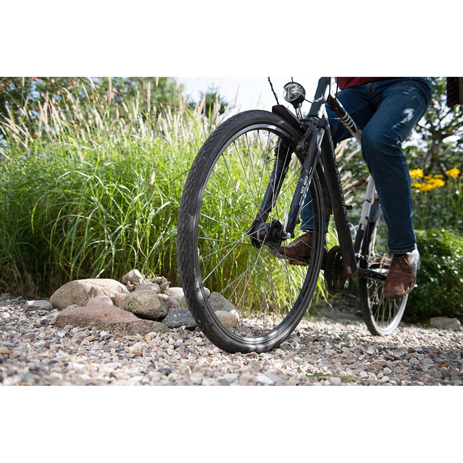 Fahrrad fährt über mit ACO Self® Kieswabe eco S befestigten Zierkiesweg im Garten.