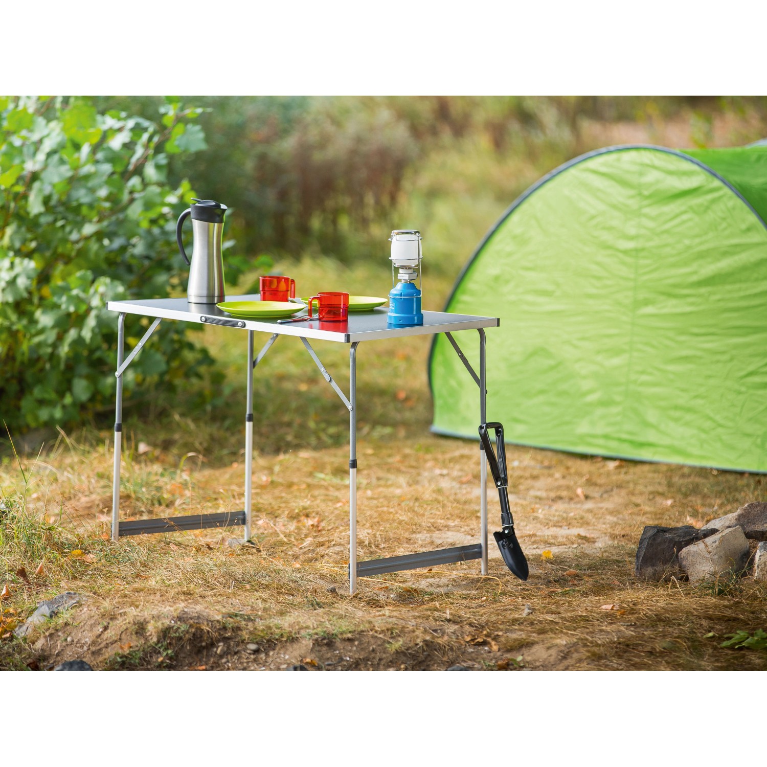 LUX Multifunktionstisch Comfort im Outdoor-Einsatz mit Geschirr und Lampe vor einem Zelt.