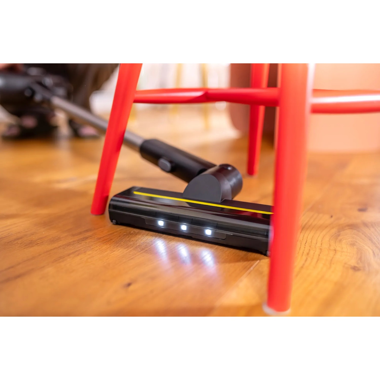 Kärcher Akku-Staubsauger VCS 3 Nano Complete Bodendüse mit LED-Lichtern unter rotem Stuhl.