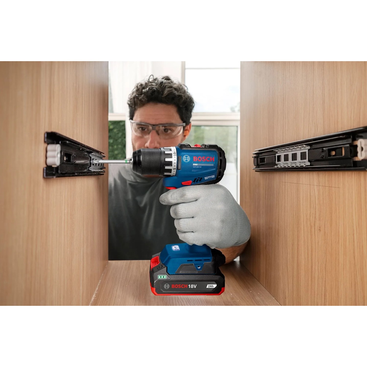Mann schraubt mit blauem Bosch Professional Akku-Bohrschrauber GSR18V-52 in Holzschrank. Kompaktes 18V Akkugerät.