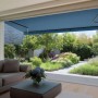Halbkassettenmarkise Reno, 3x2 m, anthrazit mit blauem Stoff, montiert an einem Haus mit Blick in den Garten.