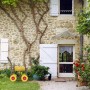 Gelber Relaxdays Gartenschlauchwagen aus Stahl mit 4 roten Rädern im Garten vor Steinhaus. Mobil, mit Handkurbel.