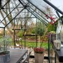 Halls GardenRoom Gewächshaus Set, 12,9 m², grün, mit Fundamentrahmen, eingerichtet mit Tisch und Pflanzen.