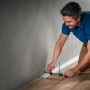 Mann nutzt wolfcraft Einpass-Set für Laminat/Designboden an Wand, um Boden zu verlegen.