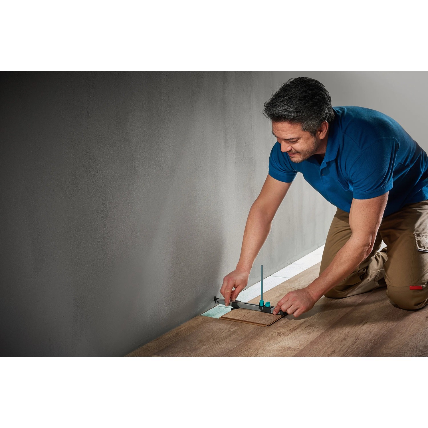 Mann nutzt wolfcraft Einpass-Set für Laminat/Designboden an Wand, um Boden zu verlegen.