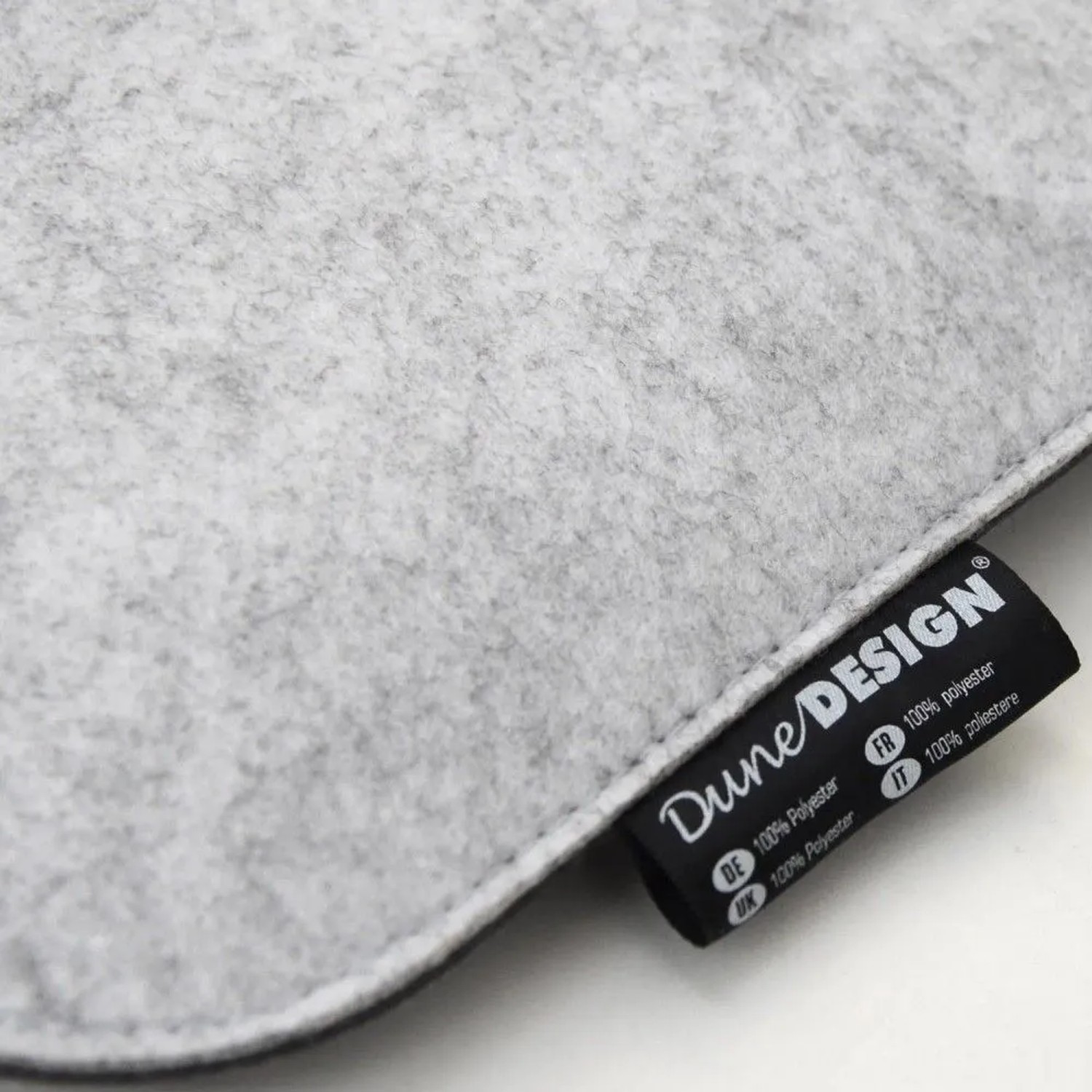 Nahaufnahme eines hellgrauen DuneDesign Filz-Sitzkissens. Die weiche Polyester-Oberfläche und das Markenetikett sind sichtbar.