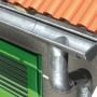 Silberne Dachrinne aus Metall an einem Haus mit grünen Fensterläden und roten Ziegeln.