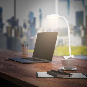 Weiße Briloner LED-Klemmleuchte PLEGG am Schreibtisch mit Laptop und Kaffeetasse.