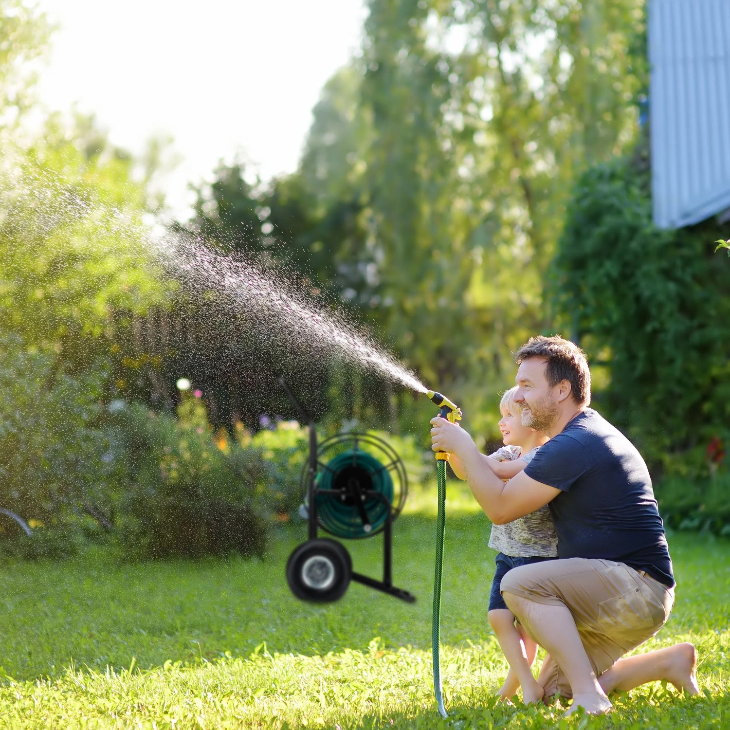 Mann und Kind bewässern Garten. Schwarzer Relaxdays Gartenschlauchwagen aus Metall/Kunststoff mit grüner Rolle.